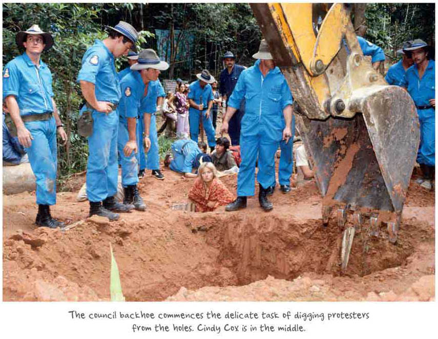 The council backhoe commences the delicate task of digging protestors from the holes. Cindy Cox is in the middle.